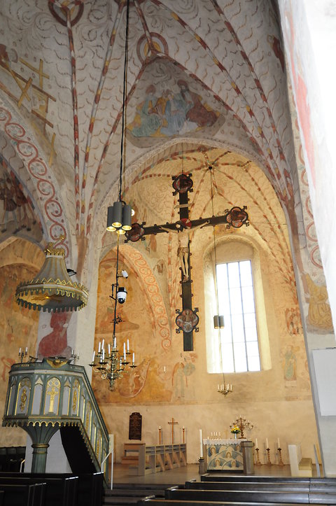 Lohjan Pyhän Laurin kirkko sisältä. Holvikaarissa paljon maalauksia ja etualalla suuri puinen krusifiksi.