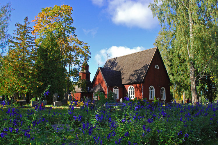 Sammatin kirkko ulkoa kesällä. Etualalla kukkii sinisiä kukkia