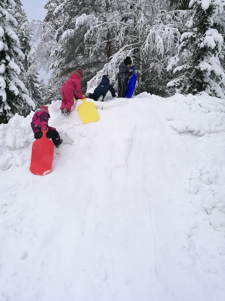 Lapset kiipeävät liukureiden kanssa ylös lumista mäkeä.