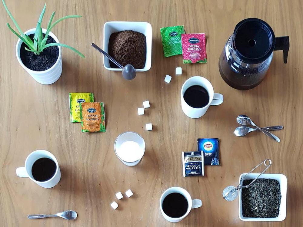 Kahvia, teetä, sokeripaloja, kahvipannu, kolme kuppia kahvia ja maitolasi pöydällä.