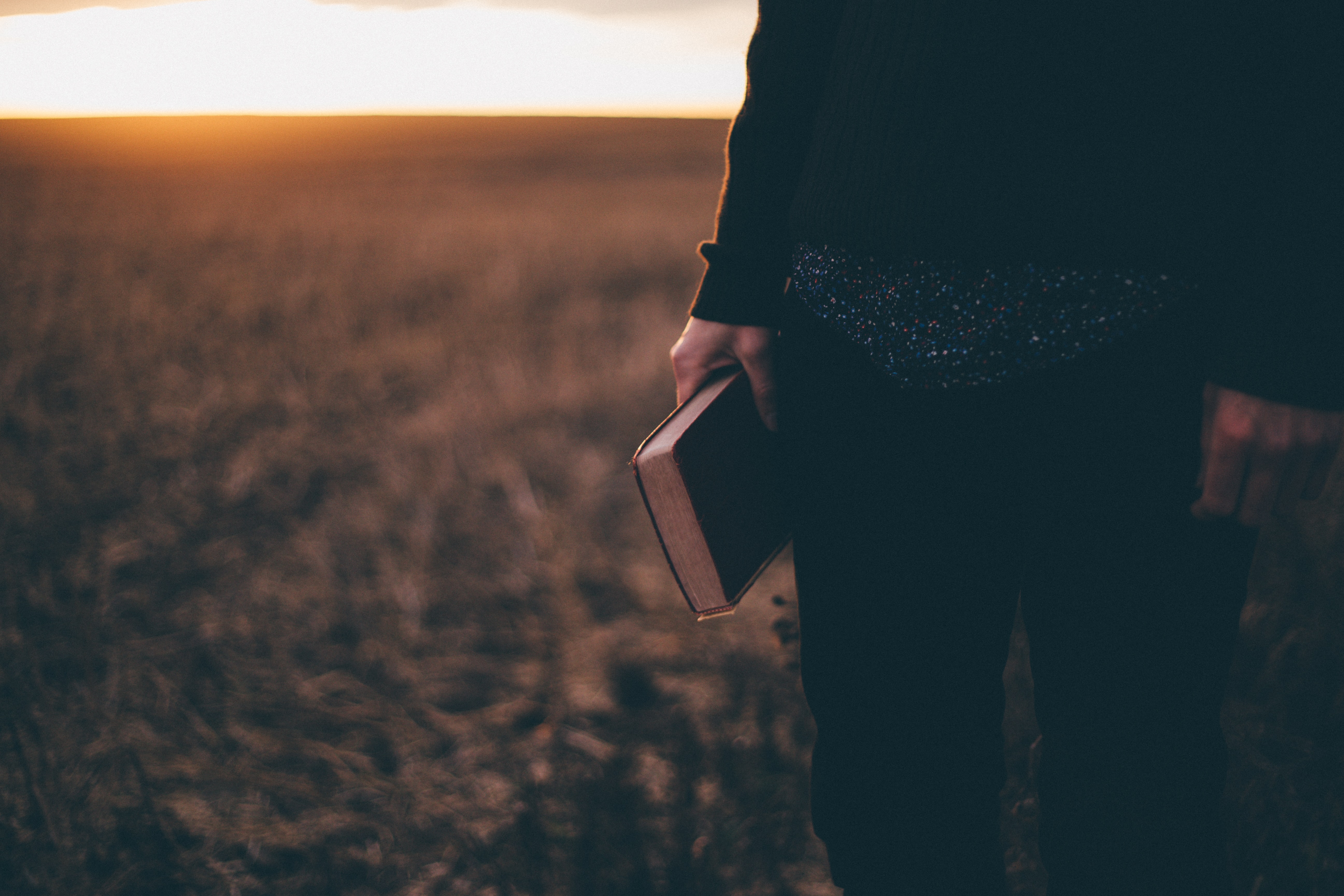 Keltaisen viljapellon edessä seisoo nainen raamattu kädessä